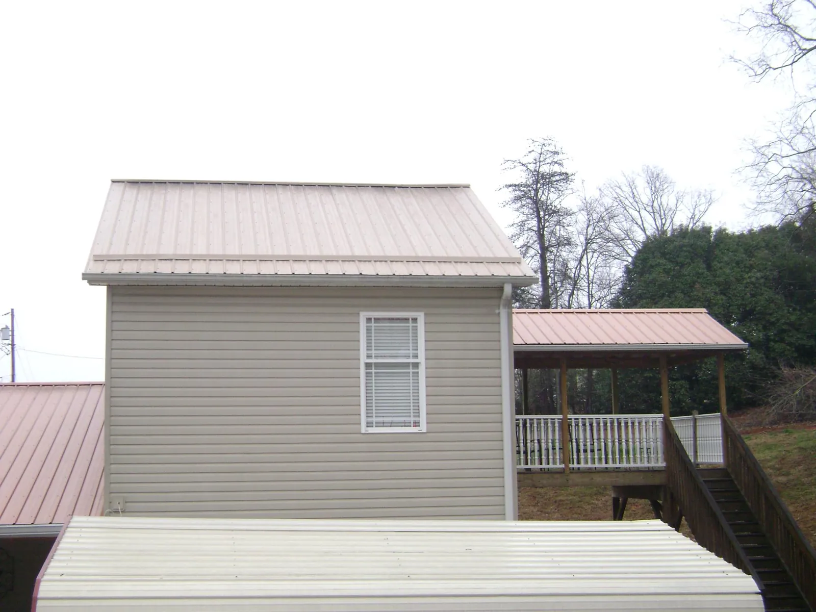 Tan metal roofs on a two story addition and attached porch, from a Roof Replacement job in Shelby